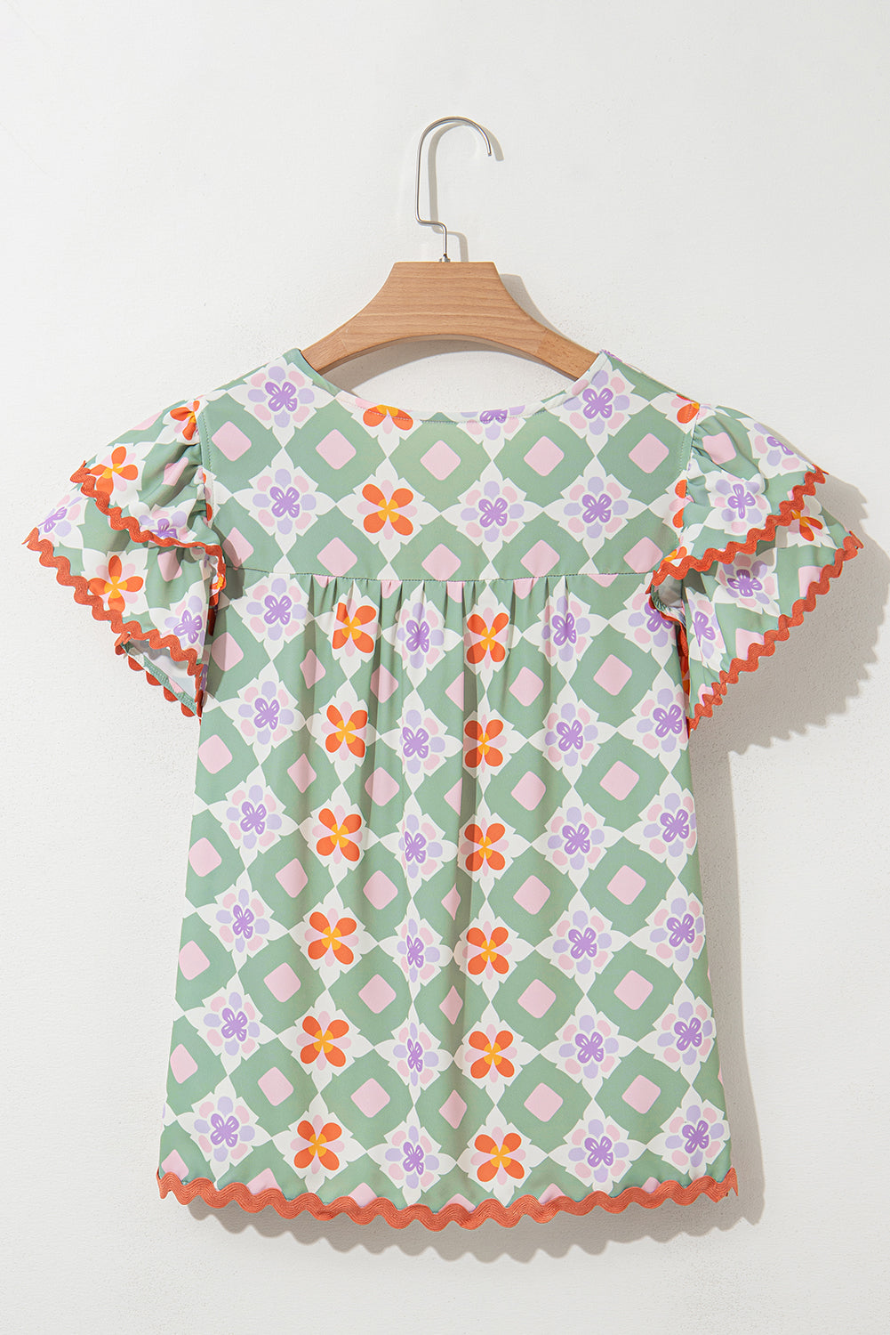 Blusa verde con estampado floral geométrico, manga con volantes escalonada, cuello en V y ribete de ric rac