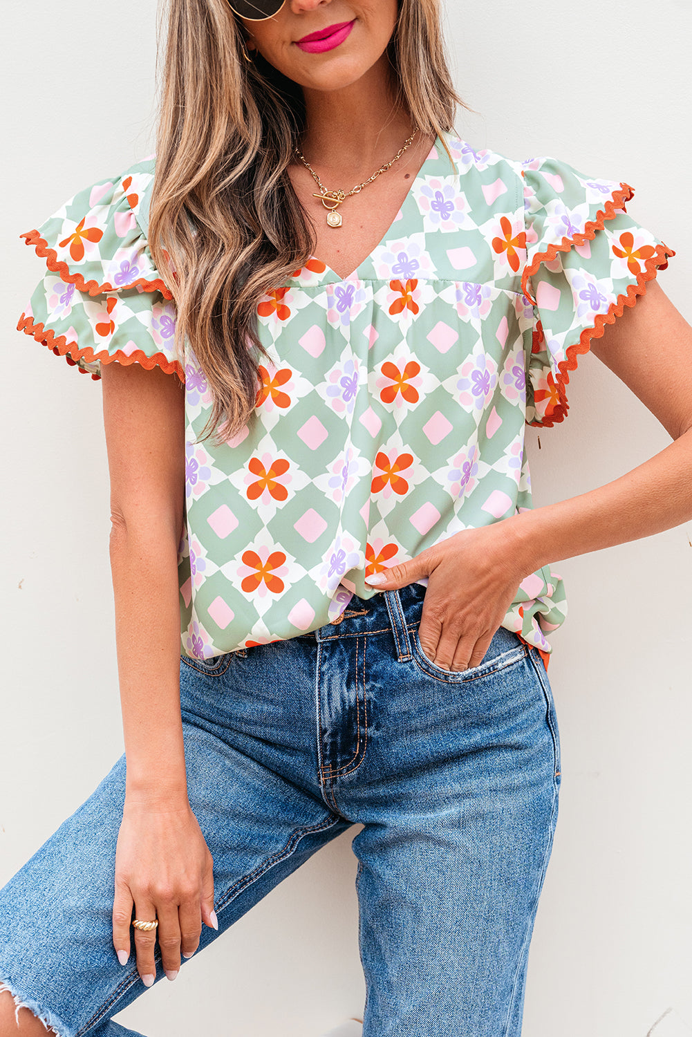 Blusa verde con estampado floral geométrico, manga con volantes escalonada, cuello en V y ribete de ric rac