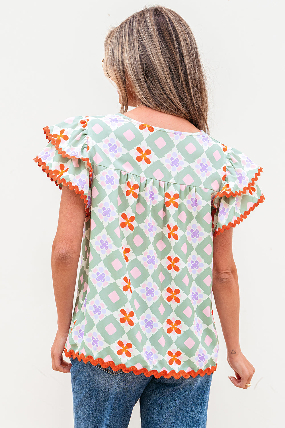 Blusa verde con estampado floral geométrico, manga con volantes escalonada, cuello en V y ribete de ric rac