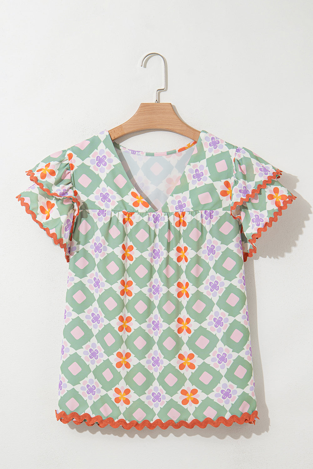 Blusa verde con estampado floral geométrico, manga con volantes escalonada, cuello en V y ribete de ric rac