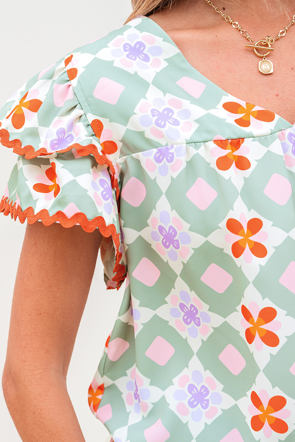 Blusa verde con estampado floral geométrico, manga con volantes escalonada, cuello en V y ribete de ric rac