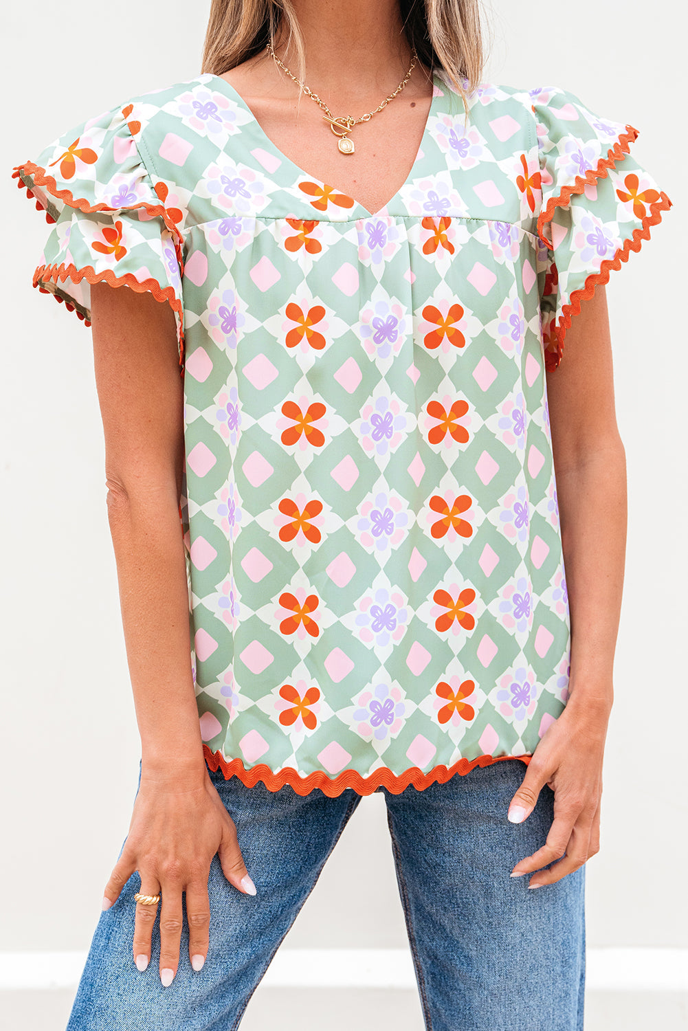 Blusa verde con estampado floral geométrico, manga con volantes escalonada, cuello en V y ribete de ric rac