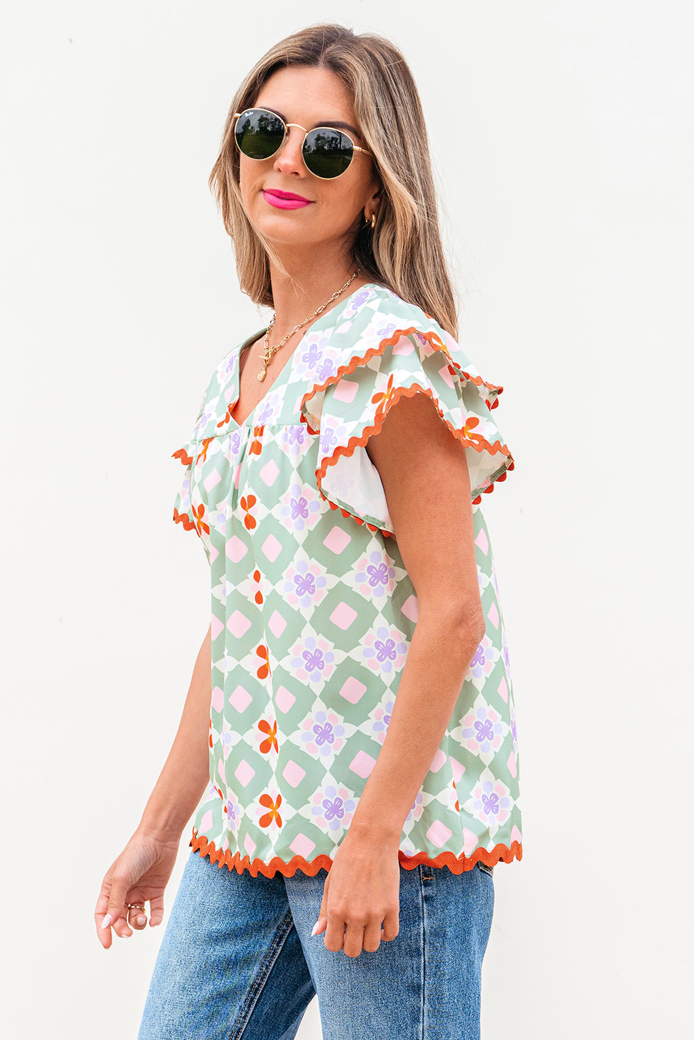 Blusa verde con estampado floral geométrico, manga con volantes escalonada, cuello en V y ribete de ric rac