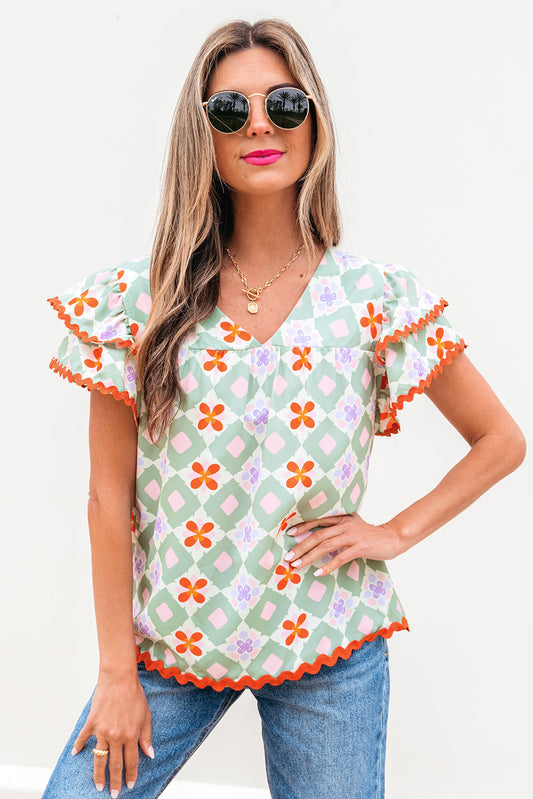 Blusa verde con estampado floral geométrico, manga con volantes escalonada, cuello en V y ribete de ric rac